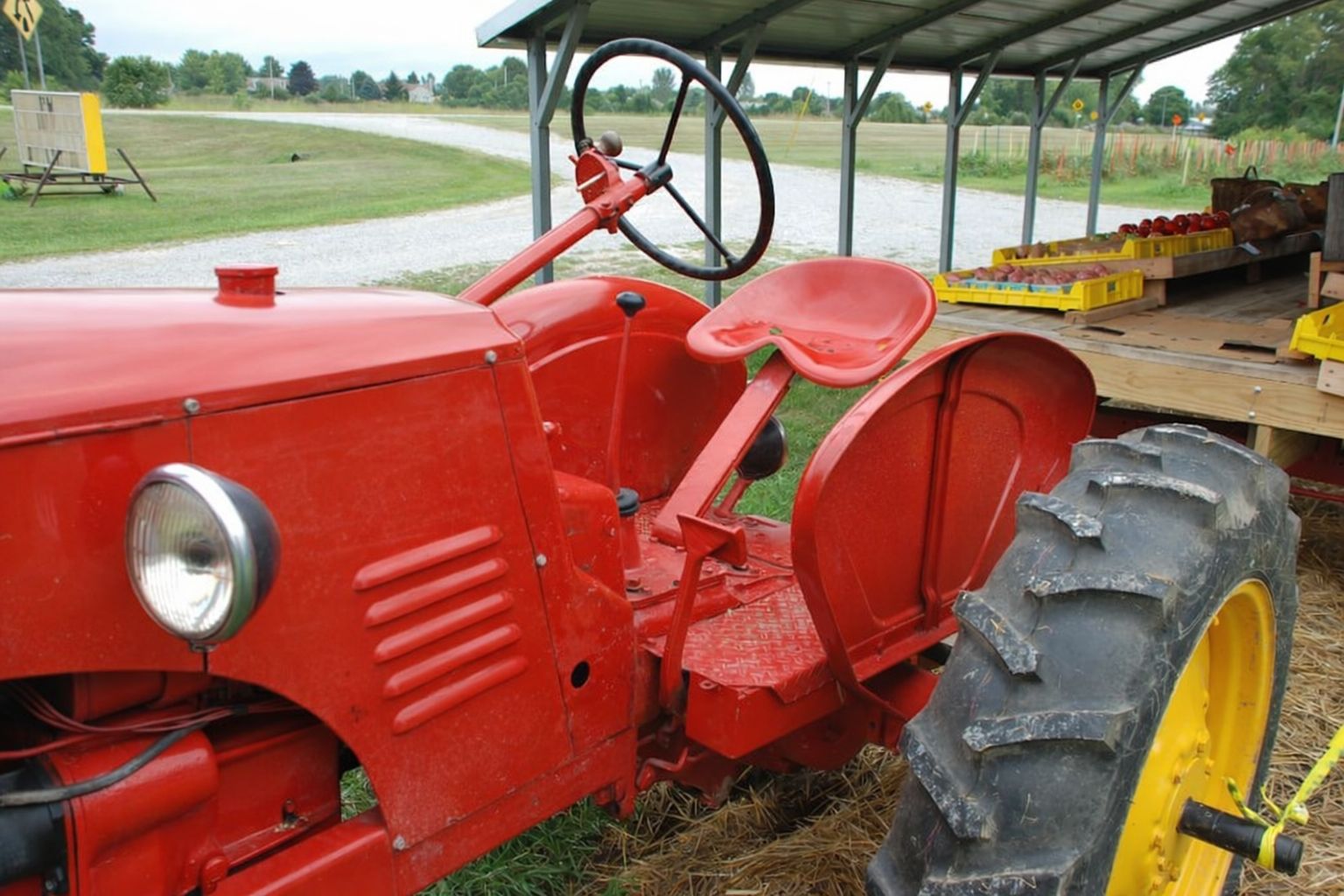 Röd traktor och varor på ett marknadsstånd under ett skjul, redo för ägarbyte.