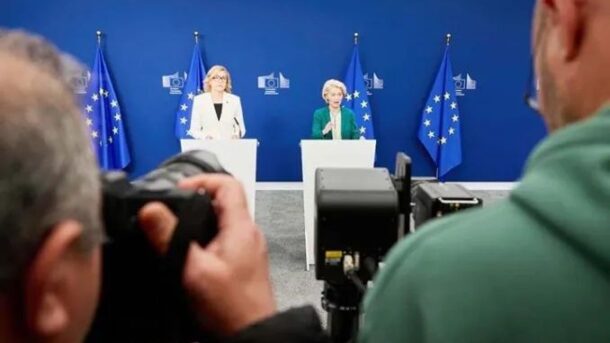 Presskonferens med EU-flaggor och fotografer framför talarstolar